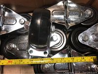 Close-up photo of multiple hard rubber casters with a measuring tape showing the 3 inch diameter wheel size.