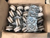 Box containing 20 white nylon swivel wheel castors with metal mounting plates, showing assembled condition and visible dirt marks on wheels.