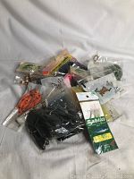 Photo showing multiple assorted fishing lures, some loose and some in original plastic packaging, including a Sabiki rig and soft plastic baits in black and orange colors.