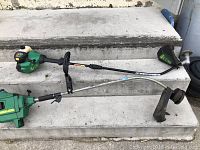 Two gas weed eater edge trimmers placed on concrete steps, showing full length of both units.