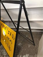 Black metal A-frame sidewalk sign holder showing side profile and sign attached