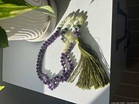 Amethyst and jade bead mala necklace coiled on surface showing tassel