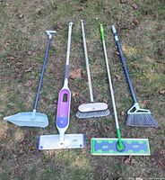 All six long-handled cleaning tools laid out on grass