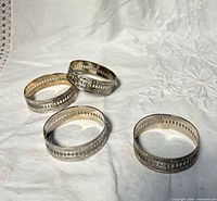 All four napkin rings displayed on fabric, showing overall design and silver finish