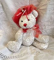 Front view of seated white plush bear with red hat and bow