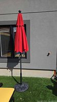 Full view of closed red patio umbrella on base