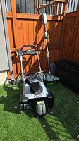 EGO multi-head tool with snow blower attachment and string trimmer leaning against fence