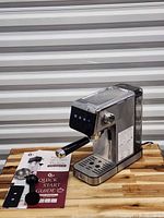 Espresso machine with portafilter attached, scoop-tamper and quick start guide on wooden surface