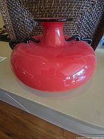 Full view of squat red glass vase with narrow neck and black rim and handles