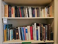Two shelves filled with assorted hardcovers, paperbacks and one spiral-bound cookbook