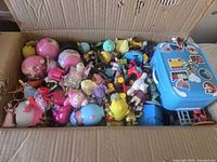 Top view of box filled with assorted small toys, eggs, figures, vehicles and blue case