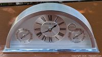 Front view of arched chrome Howard Miller desk clock showing all three dials