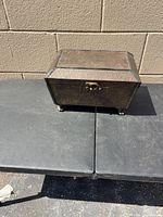 Closed jewelry box showing embossed metal exterior, latch, and claw feet