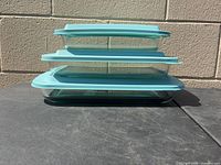 Side view of three nesting rectangular glass containers with aqua lids
