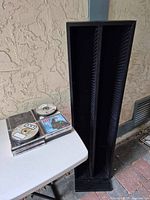 CD tower and a stack of jewel cases with loose discs on table
