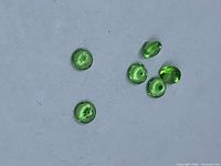 Six vivid green round tsavorite garnets face-up on neutral background