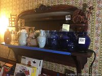 Wide angle showing wooden shelf with attached mirror, decorative carving on top, holding various glassware items.