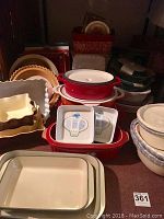 General view of assorted baking dishes including red enameled, beige ceramic, stacked pie dishes and mixing bowls.