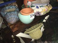 Assorted ceramic pots and planters including blue and pastel floral designs, a light green pot, and a decorative hat-shaped item displayed on a wooden folding tray table.