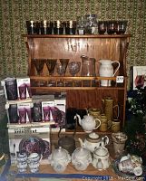 Wide shot of wooden rack holding assorted decorative glassware and ceramic pitchers and teapots.