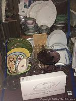 Wide view of assortment of ceramic plates, platters, and glass decor items arranged on shelf