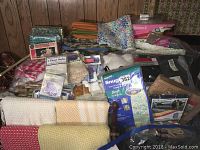 Wide overview of the lot showing folded table linens, flour sacks, ironing board covers, boxed small travel iron, and assorted textiles and sewing supplies.