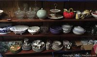 Three shelves holding various glass and ceramic dishware including candy dishes, bowls, tea cups, and decorative items.