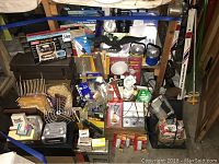 Wide view showing assortment of tools including glue gun, flashlight, packaged hardware, fans, and other miscellaneous tools stacked and arranged on a shelf.
