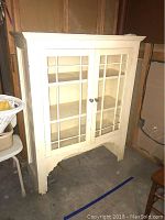White painted wood cabinet with two glass paneled doors, front view showing wear and knob details.
