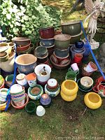 Overview photo of large varied assortment of garden pots in assorted colors and sizes arranged outdoors on grass.