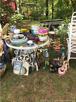 Wide view of the garden pots, planters, decorative animal sculptures, plaques, and stacked chairs outdoors on grass and dirt.