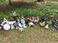 View of entire assortment of cement garden statues, sundial plaque, and decorative garden stakes arranged on grass outdoors
