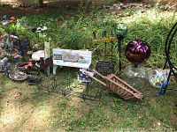 Wide view showing most garden decor items arranged on grass outdoors including gazing balls, wooden wheelbarrow, metal stakes, signs, and small figurines.