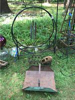 Side view of metal circular log holder with wind chimes hanging inside and small wicker basket, placed on grass outdoors.