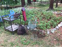 Full view of garden decor assortment and black metal rolling cart on grass with trees
