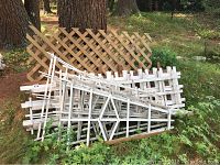 Disassembled wooden trellis panels piled outdoors near a tree, showing the worn condition and varying designs of the panels.