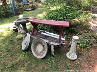 Outdoor garden scene showing red painted wooden bench stacked on faded white cedar Adirondack table bench, with large round cement decor pieces and bird bath in background.