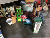 Various bird feeders, bird houses, plastic seed containers, baskets, one white ceramic planter, and several paint cans and supplies seen on the floor and in baskets.