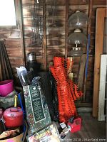 Photo showing green Deer Block protective netting packaging, orange plastic fencing rolls, assorted garden stakes or metal supports, and a double glass globe hand lantern in a rustic wooden setting.