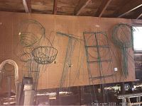 Various wire plant supports and stands of different shapes and sizes hanging on pegboard in a garage.