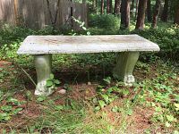 Front view of concrete garden bench in outdoor natural setting surrounded by grass and plants.