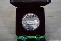 Reverse of coin showing skyline design, coin in capsule within display box