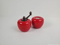 Front view of both red apple seasoners showing crank handle and perforated salt cap