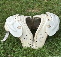 Front view of adult white football shoulder pads laid open on grass