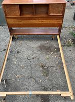 Front view of wood headboard showing cubbies, sliding doors, lower shelf, attached rails on casters