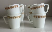 Six of the eight Pyrex mugs stacked showing floral band and handles