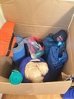 Top view of box showing sleeping bags, foam pad, bug spray, rolled mats
