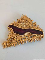 Front view showing gold-tone brutalist texture and burgundy resin center