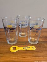 Three Corona Extra pint glasses and yellow Corona Extra bottle opener on tabletop
