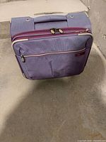 Front view of purple Chloe softside carry-on with front zip pocket and wheels visible